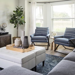 Living room with neutral blue and white furnishings, tufted ottoman coffee table