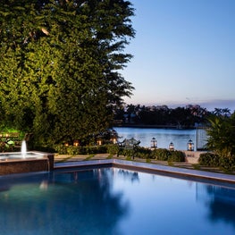 The pool, water fountain and patio overlook a natural body of water.