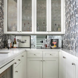 Portfolio: A home bar with white cabinets, glass inlay uppers, and abstract wallpaper.