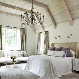 Authentic, neutral master bedroom with high, beamed ceiling