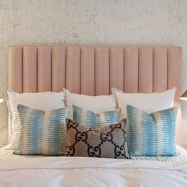 Symmetrical gold bedside lamps, upholstered headboard, patterned throw pillows.