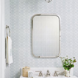 Blue and white wallpapered powder room with marble vanity and polished nickel fixtures