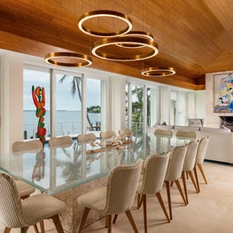 A brass chandelier suspends from a bamboo ceiling over a glass topped table.