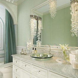 The bathroom shimmers with glass beaded wallpaper, hung above a marble wainscot.  The vanity features a mirrored-glass vessel sink and spherical glass knobs backed by mirrored plates.  Lighting is sconces and a dramatic ceiling fixture of crystal strands 