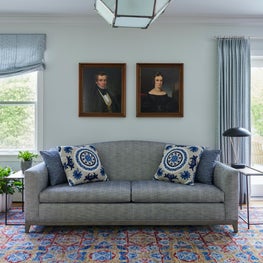 Kenilworth Living Room. Blue textured sofa with embroidered accent pillows, blue drapes, modern table lamp & oriental rug.