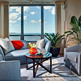 Lake Shore Drive Living Room. Blue seating area on modern Lapchi rug with lake view and orange accents.