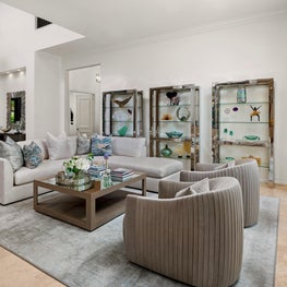 Expansive Decadent Waterfront living room, neutral, mirrored coffee table, chrome shelves, white sectional