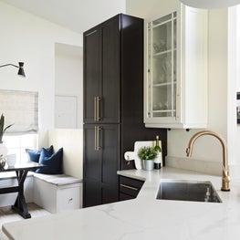 Cozy breakfast nook tucked away in black and white kitchen with brass finishes.
