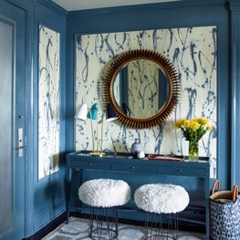 Blue foyer with paneling, console table, geometric rug, and white pouf stools