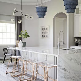 Rustic wood floors juxtaposed with modern waterfall island and pendant lighting.