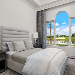 Expansive Decadent Waterfront, neutral bedroom, dark hardwood floors, picture window, crown molding, light gray rug, tall gray curtains
