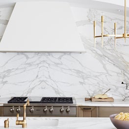 Oversized marble backsplash and white hood in a contemporary kitchen with brass accents