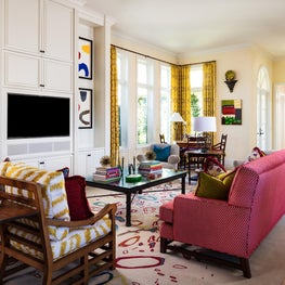 Colorful area rug grounds yellow patterned draperies and colorful furniture. 