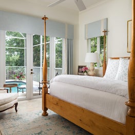 This neutral bedroom has a four post bed grounded on a blue patterned area rug.