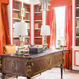 This glamorous library features lacquered walls in brilliant white & orange echoed by bright fabrics from Jim Thompson. Layers of books and antique furniture create a posh setting for the new neoclassicist. Designers: Summer Loftin and Marcia Sherrill