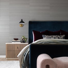 Portfolio: A velvet upholstered bed stands before a textured wallcovering, while sculptural sconces and layered textiles add depth and contrast.