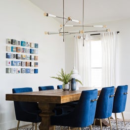 White wall w/ vibrant blue dining chairs, blue rug, custom art & modern lighting