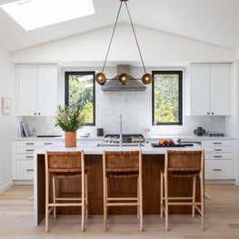 Kitchen with woven leather bar stools, white square tile backsplash, and white cabinets