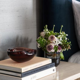 Portfolio: A vignette of the bedroom pairs a reeded wood nightstand with a stone top, layered books, fresh florals, and warm brass accents.