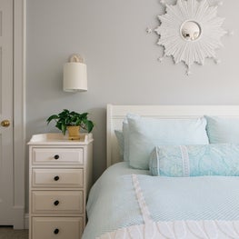 Glenview Bedroom. Light blue and grey room with small print bedding, white accents & a nautical statement mirror.