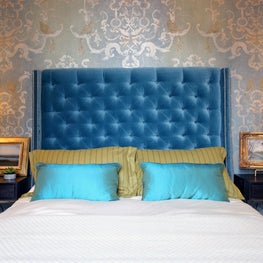 Traditional master bedroom with ornate wallpaper and blue tufted headboard