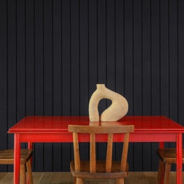 Dining area with sleek red table, black paneled walls, objet d'art centerpiece