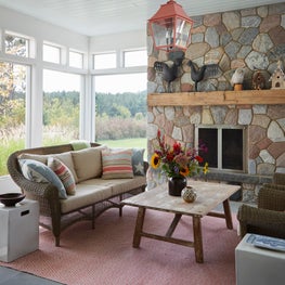 Three Barn Farm Sunroom. Rock fireplace with pendant lantern and rustic farm-inspired decor.