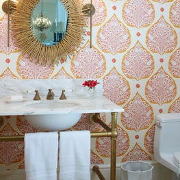 Colorful modern powder room with wall paper, brass mirror, brass sconces, brass washstand and marble