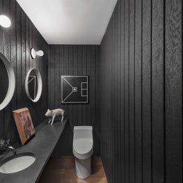 Sleek bathroom with black paneled walls, lightbulb sconces, round mirrors