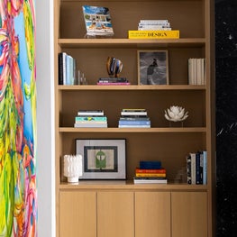 Portfolio: A living room vignette features white oak shelving styled with books, artwork, and decorative accessories above concealed storage.