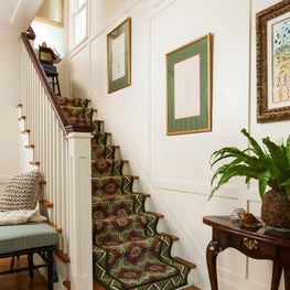 White walls, wood floors and a patterned colorful runner complete the entryway.