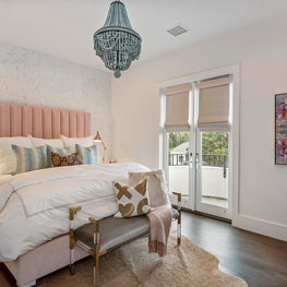 Blush upholstered bed enhanced by blue beaded chandelier & lucite w/ gold bench