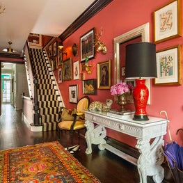 Eclectic foyer with coral walls, gallery wall art, & striped stair runner