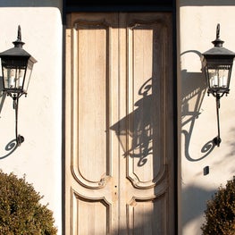 Natural Wood French Country Double Front Door in a Stucco Wall with Gas Lanterns