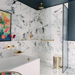 Marble Bathroom with abstract art, reeded glass panel, and brass fixtures 