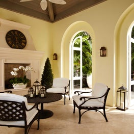 The cabana has a decorative fireplace and white cushioned wrought iron chairs.