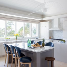 Portfolio: A modern white kitchen with white range hood, dual islands, and blue stools in Pebble Beach, CA.