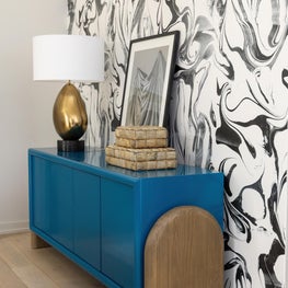 Portfolio: A vibrant blue console stands against a black-and-white feature wall, with brass lighting and unique artwork.