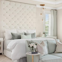 Dramatic tufted headboard w/ soft, white & mint furniture, gold finishes.
