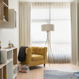 Modern guest bedroom with yellow chair, floor lamp, and white curtains