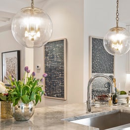 Glamorous open kitchen with wall art, pendant lighting & marble countertops.
