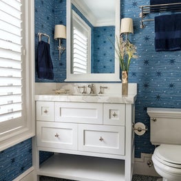 This white powder room showcases bold blue patterned wallpaper and vibrant floor tiles.