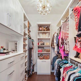 Large walk-in closet with customer cabinetry & contemporary gold light fixtures.