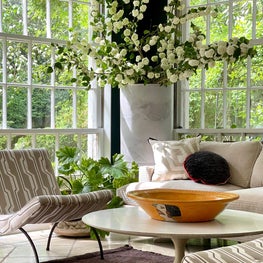 Sun-filled corner of a sunroom seating arrangement with iconic pieces of Midcentury furniture and neutral geometric JIM THOMPSON fabrics.