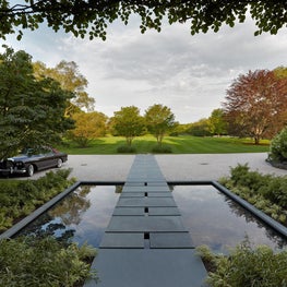 The entry to the home crosses a reflecting pool surrounded by planting.