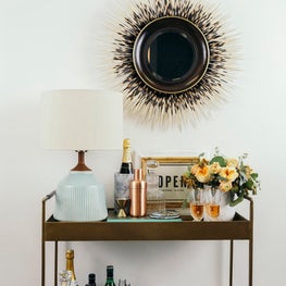 Welcoming bar cart with custom porcupine mirror and mid-century table lamp