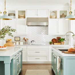 Mint green kitchen with hanging pendants marble counter tops and painted island with rattan counter stools