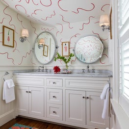 Whimsical powder room with bright patterned rug and white painted walls with red swirls.