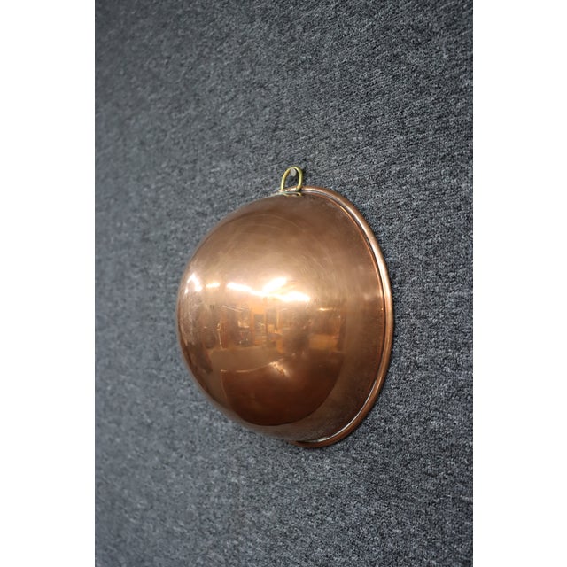 English copper mixing bowl with a rounded form, rolled rim, and brass hanging loop. Stamped "Made in England," this piece...
