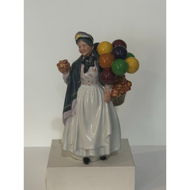 A delightful Royal Doulton “Biddy Penny Farthing” figurine (HN 1843) depicting a cheerful street vendor carrying a bundle...